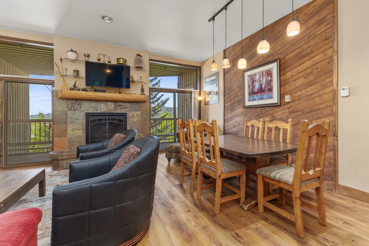 A cozy living and dining space featuring a prominent stone fireplace, a welcoming dining table, and stylish hanging lights. The room glows with warmth and offers a clear view of multiple zones for gathering and entertainment.