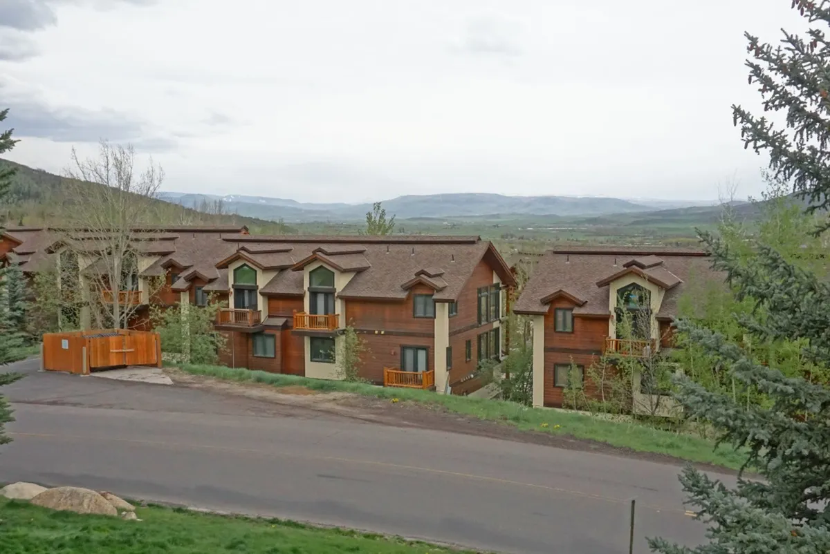 A broad exterior view showcasing townhouse buildings nestled among trees with a majestic mountain backdrop. The scene conveys the immersive natural surroundings and easy access to outdoor adventures.