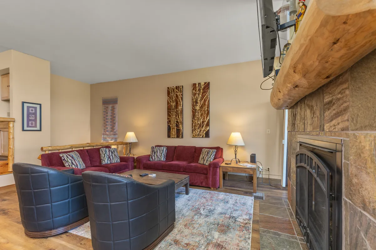 A large, welcoming living space with red sofas and black leather chairs arranged around a fireplace. The area is accented by vibrant artwork and offers plenty of seating for groups to gather, socialize, and relax together. The layout suggests a perfect spot for evening gatherings, movie nights, or lively conversation.
