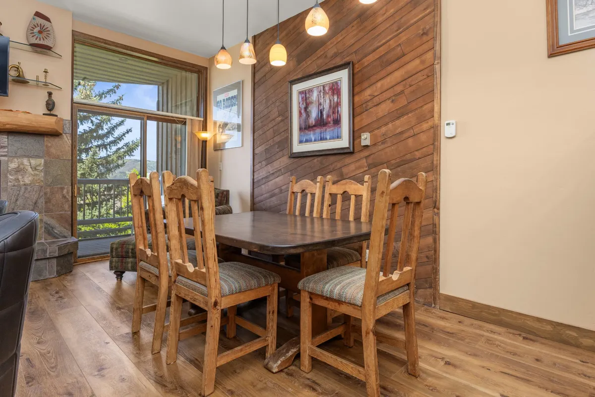 A wooden dining table with suspension lights overhead and a textured feature wall, set in a space designed for group meals and celebrations. The setup is ideal for family-style dining, festive dinners, or simply gathering to share stories and meals.