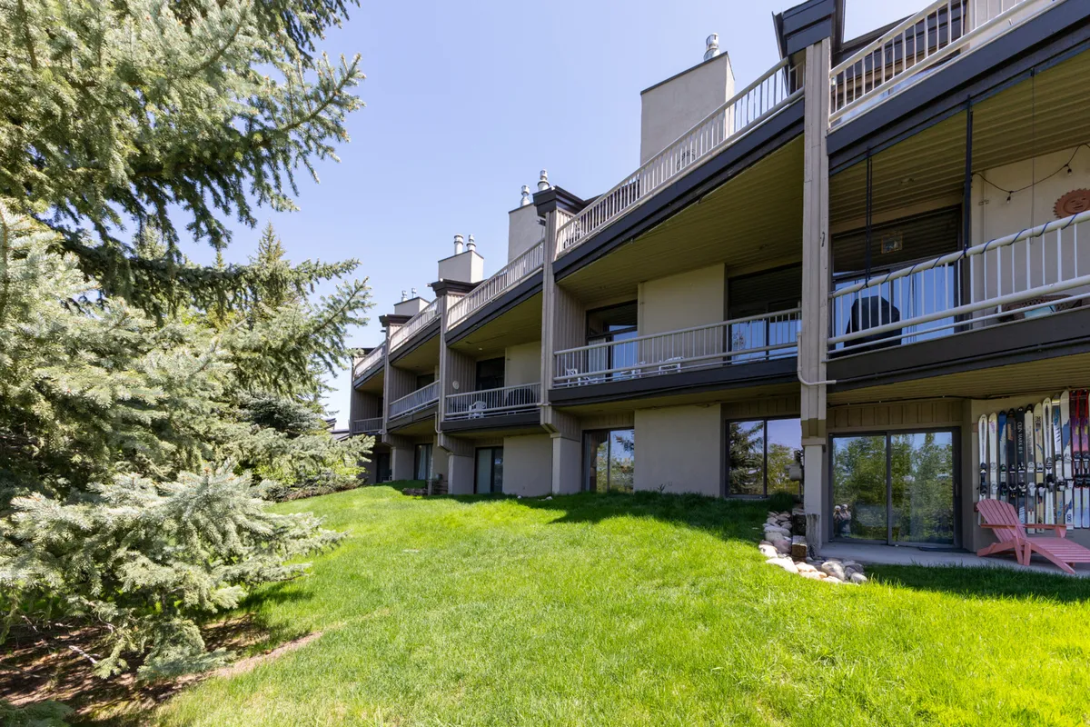 This exterior image features balconies overlooking a green lawn, shaded by mature trees. The scene conjures a sense of community and outdoor living, with spaces that are perfect for relaxing with friends, enjoying meals, or simply soaking up the summer atmosphere.