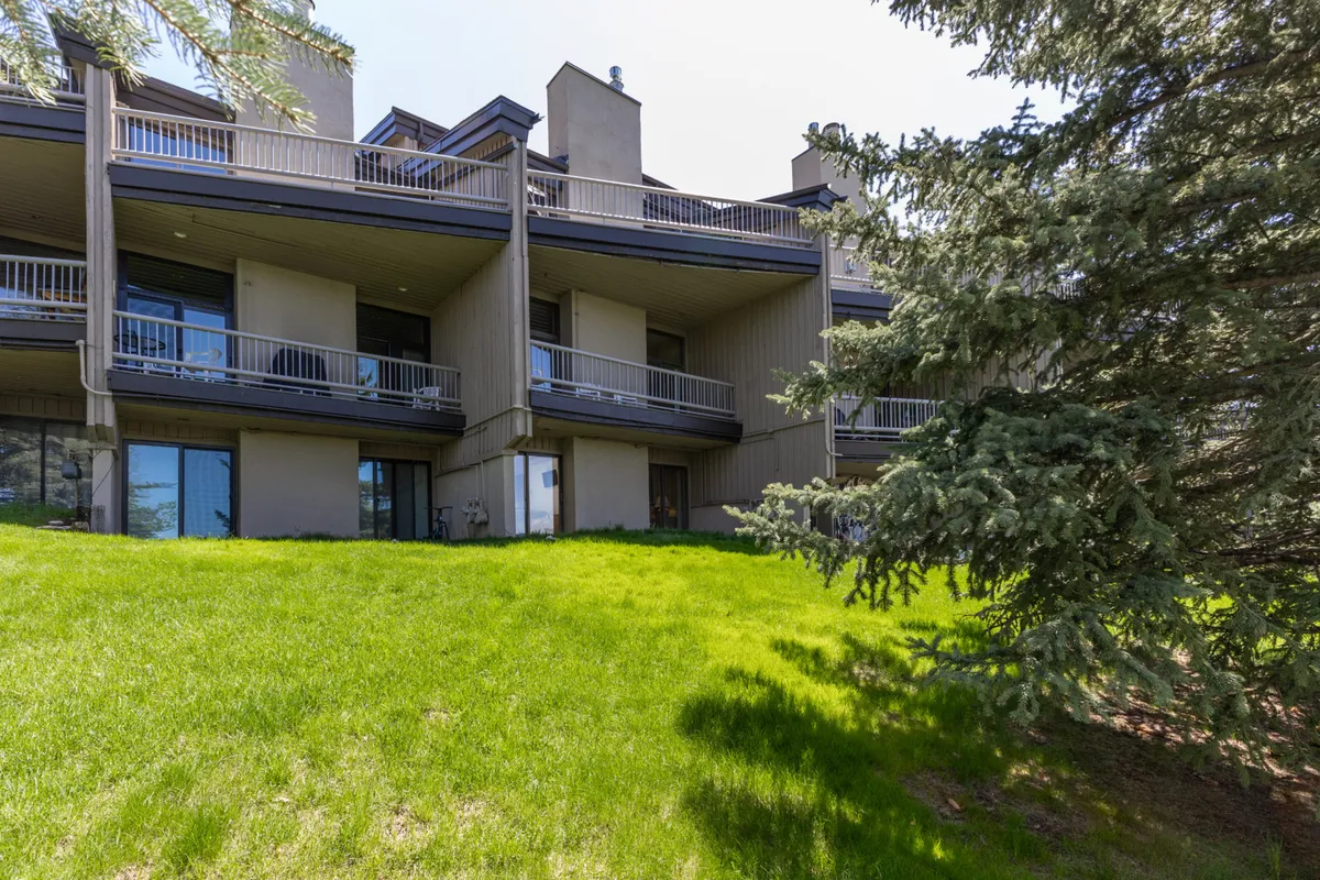 This exterior image shows balconies overlooking lush green grass and mature trees, suggesting a tranquil setting for relaxation, socializing, or taking in mountain views. The presence of balconies reinforces the idea of outdoor living and access to fresh air.