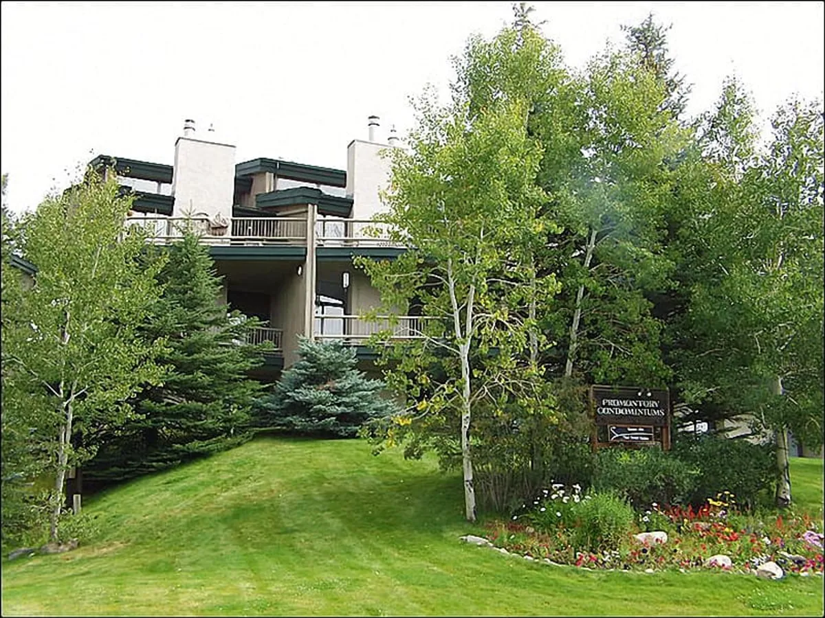 The exterior view showcases the building facade against a tree-lined backdrop, with landscaped gardens and visible signage. The scene conveys a welcoming and communal atmosphere—ideal for enjoying shared amenities like the pool and hot tub.