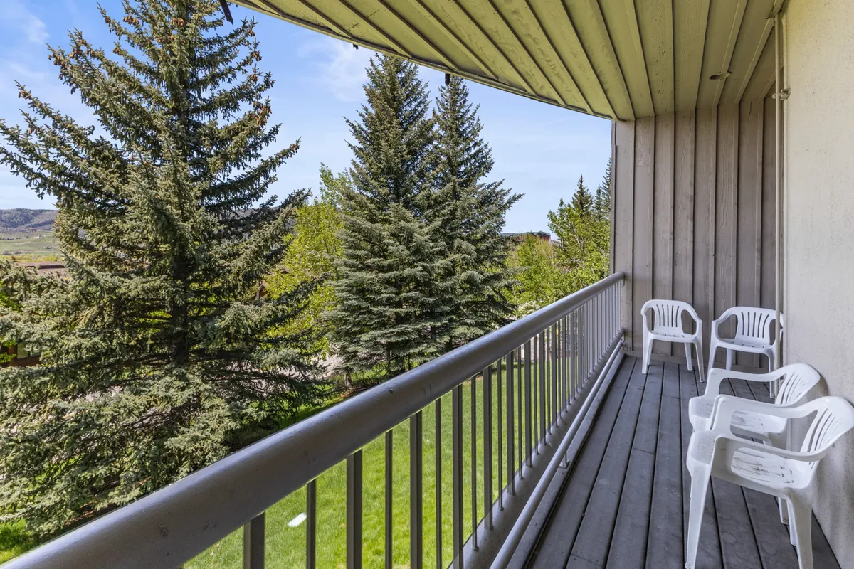 A shaded outdoor balcony with comfortable seating overlooks lush trees, inviting guests to relax, read, or simply enjoy the mountain air. The calm atmosphere highlights natural cooling and a connection with the outdoors.