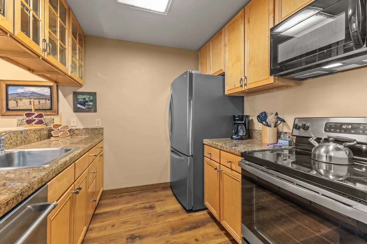 A showcase of the kitchen's quality finishes, with granite countertops, stainless steel appliances, and wooden cabinetry. The open layout hints at the adjacent social areas, while the kitchen itself is clearly equipped for group cooking and entertaining.