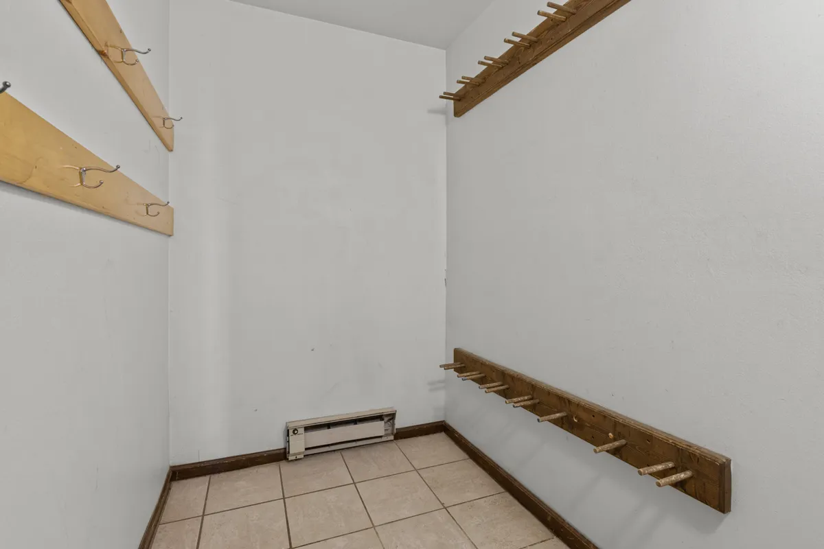 A practical storage area with wooden hooks on the wall and a tiled floor, designed for efficient organization of outdoor gear like coats, skis, or bikes. The plain walls keep the focus on functionality.