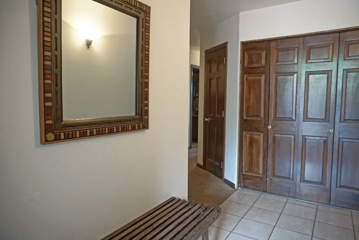 This image features a welcoming entryway with a decorative mirror, a sturdy wooden bench for sitting or organizing gear, and closed closet doors along the wall. The space is both functional and inviting, setting the tone for arrivals and departures.